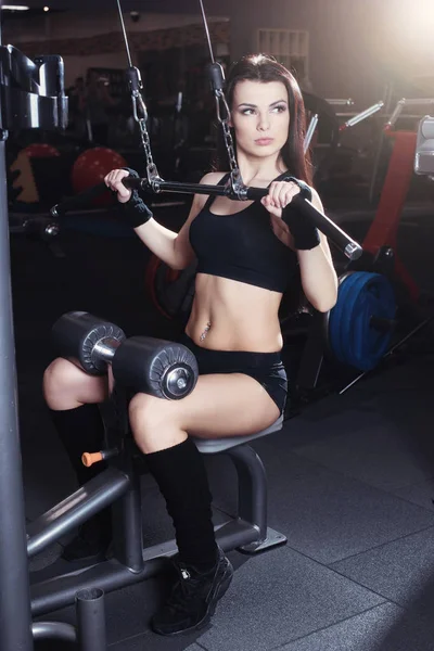 Izmos barna fitness lány csinál gyakorlatok az edzőteremben. Súlyemelés a gépen a testépítők, fitness lány. — Stock Fotó