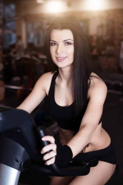 Spor salonunda kondisyon bisikletleri üzerinde spor eğitim giyen kaslı genç kadın. Yoğun kardiyo egzersiz. — Stok fotoğraf