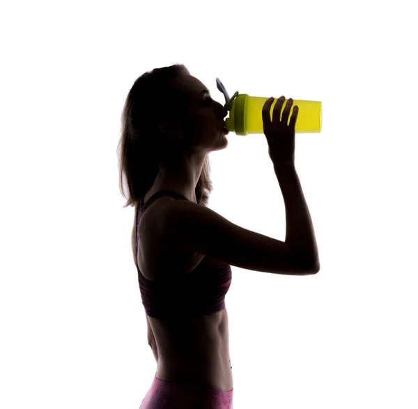 Щаслива спортивна жінка, яка п'є з пляшки зеленого струсу в студії. Силуетне фото. Ізольовані на білому тлі . — стокове фото
