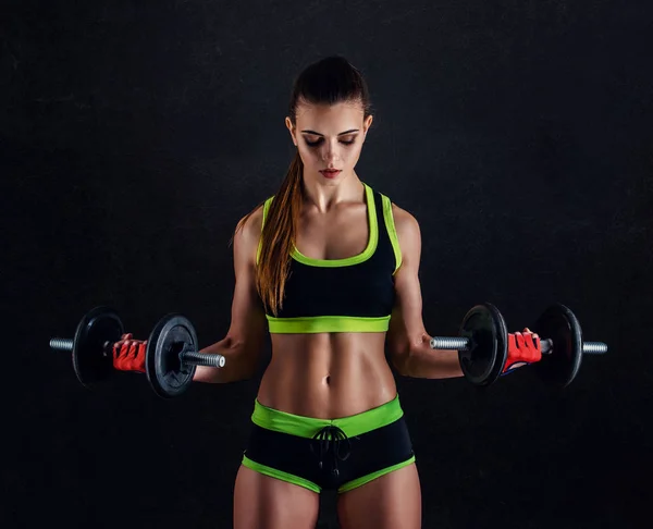 Mujer atlética joven en ropa deportiva con mancuernas en estudio sobre fondo negro. Figura deportiva femenina ideal. Chica fitness con cuerpo musculoso esculpido perfecto y apretado . —  Fotos de Stock