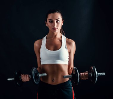 Atletik genç kadının siyah arka plan karşı bir fitness egzersiz yapması. Çekici fitness kız dumbbells ile kas pompalama.