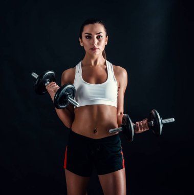 Atletik genç kadının siyah arka plan karşı bir fitness egzersiz yapması. Çekici fitness kız dumbbells ile kas pompalama.