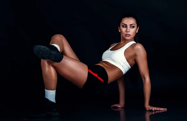 Mujer joven atlética haciendo un entrenamiento de fitness sobre fondo negro. Mujer deportiva en ropa deportiva con un cuerpo de fitness perfecto . —  Fotos de Stock