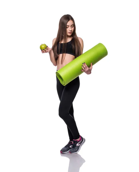 Ritratto di giovane donna sorridente che tiene arrotolato esercizio yoga mat e mela verde isolato su sfondo bianco . — Foto Stock