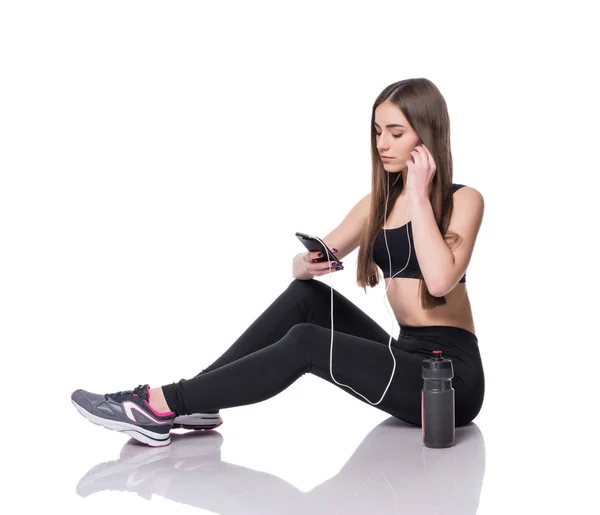 Πορτρέτο μιας γυναίκας νεαρός αθλητής να ακούτε μουσική με ακουστικά σε λευκό φόντο. Κορίτσι ελκυστικό γυμναστήριο κουβεντιάζοντας σε smartphone ιόντων στούντιο. — Φωτογραφία Αρχείου