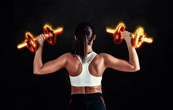 Mujer joven atlética haciendo un entrenamiento de fitness sobre fondo negro. Atractiva chica fitness bombeando músculos con mancuernas . —  Fotos de Stock