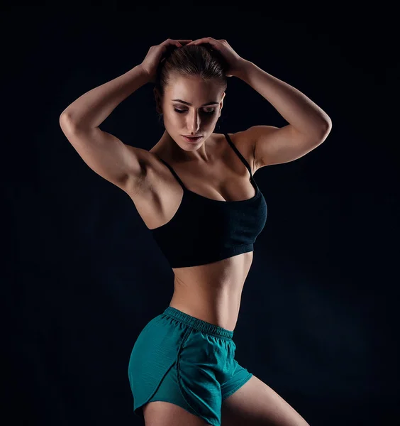 Chica joven deportiva en ropa deportiva que muestra los músculos en el fondo negro. Mujer atlética joven bronceada. Un gran deporte cuerpo femenino . —  Fotos de Stock