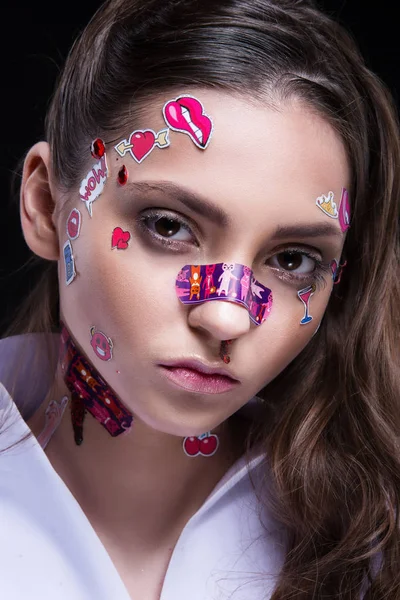 Hermosa chica de moda con maquillaje profesional de lujo y divertidas pegatinas emoji pegadas en la cara . — Foto de Stock