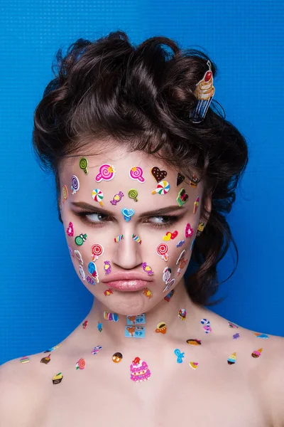 Güzel moda kız lüks profesyonel makyaj ve komik emoji çıkartmaları yüzünde yapıştırılmış. Cupcake elinde olan kadın. — Stok fotoğraf