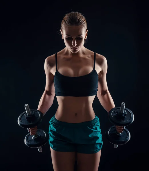 Portret van een jonge fitness vrouw in sportkleding training met halters op zwarte achtergrond. Gebruinde sexy atletische meisje. Een grote sportieve vrouwelijk lichaam. — Stockfoto