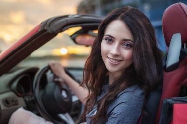 Gün batımında lüks kırmızı cabriolet otomobil sürüş oldukça genç esmer kadın.