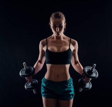 Spor giyim siyah arka plan üzerine dumbbells ile egzersiz yapıyor bir genç fitness kadın portresi. Yanık tenli seksi atletik kız. Harika bir sportif kadın vücudu.