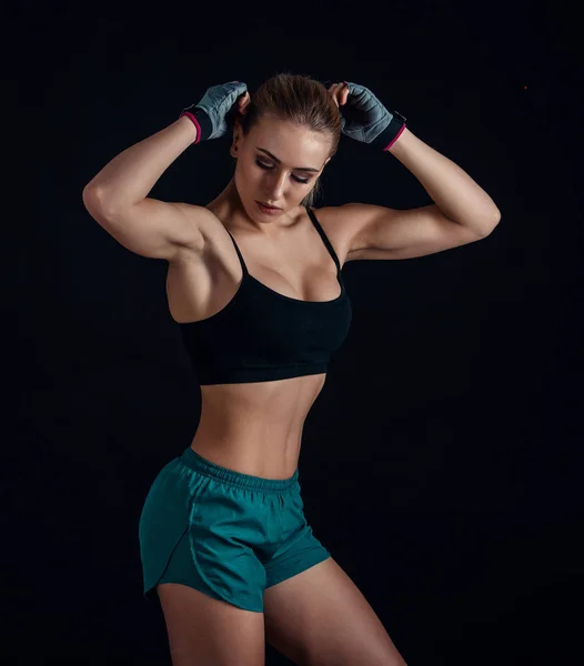 Спортивная молодая девушка в спортивной одежде показывает мышцы на черном фоне. Загорелая молодая спортсменка. Великолепное женское тело . — стоковое фото