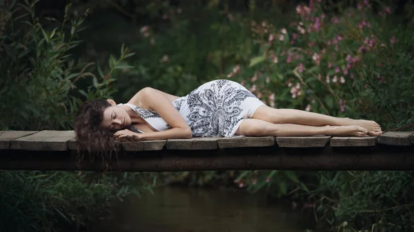 美丽的年轻女子躺在桥上森林河. — 图库照片