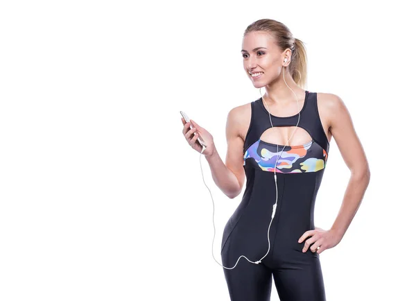 Felice fitness giovane donna che indossa tuta sportiva con auricolari sta ascoltando la musica utilizzando uno smartphone . — Foto Stock