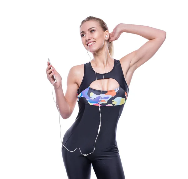 Happy fitness jovem mulher vestindo sportswear tracksuit com fones de ouvido está ouvindo música usando um smartphone . — Fotografia de Stock