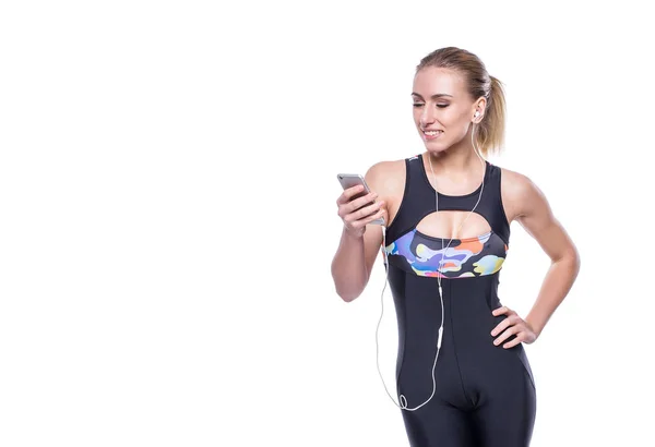 Happy fitness giovane donna che indossa tuta sportiva con auricolari sta ascoltando la musica utilizzando uno smartphone. Copyspace per testo . — Foto Stock