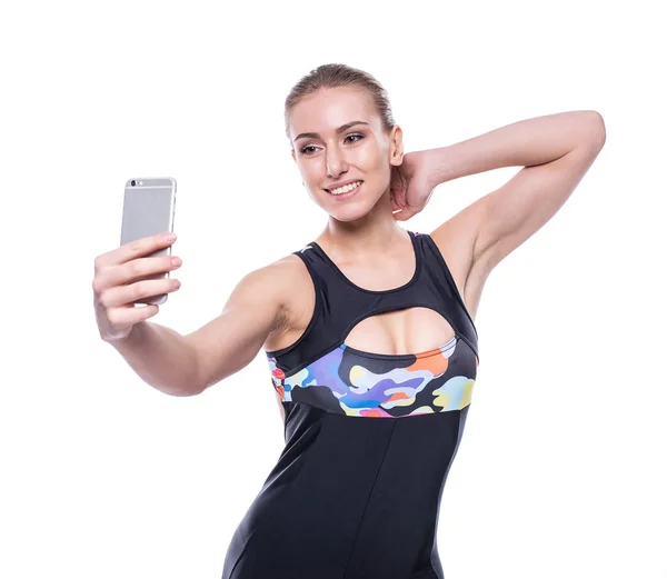 Felice fitness giovane donna che indossa tuta sportiva sta prendendo selfie con il suo telefono cellulare isolato su sfondo bianco . — Foto Stock