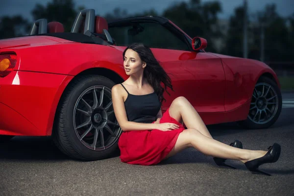 Yere yakın lüks kırmızı cabriolet otomobil tekerlek üzerinde oturan sevimli genç esmer kadın.