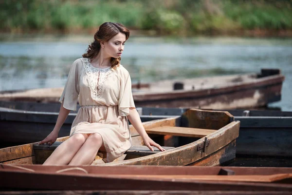 Portrait of pretty young woman sitting in the boat on river bank. — Stock Photo, Image