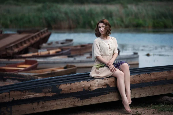 Portrait of pretty young woman sitting in the boat on river bank.