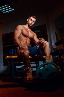 Vücut geliştirmeci bir ağırlık bankta oturur, o ara verirler. Bir spor salonu ve kameraya gülümseyen iş yerinde kas adam.