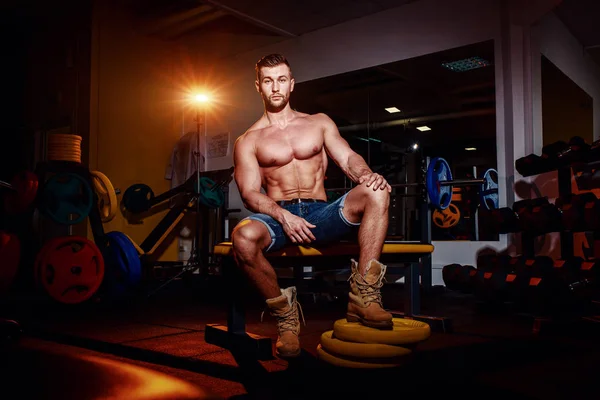 Vücut geliştirmeci bir ağırlık bankta oturur, o ara verirler. Bir spor salonu ve kameraya gülümseyen iş yerinde kas adam.