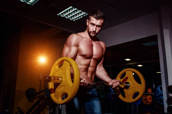 Atlético joven haciendo ejercicios con barra de pesas en el gimnasio. Guapo musculoso culturista chico está haciendo ejercicio . — Foto de Stock