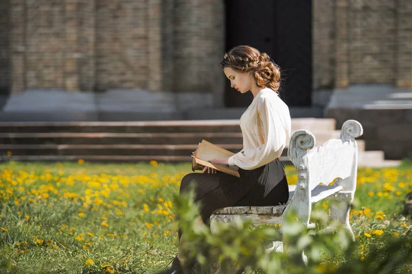 Retro portrait of a beautiful dreamy girl reading a book outdoors. Soft vintage toning. — Stock Photo, Image