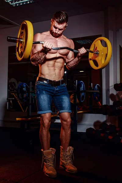 Atlético joven haciendo ejercicios con barra de pesas en el gimnasio. Guapo musculoso culturista chico está haciendo ejercicio . —  Fotos de Stock