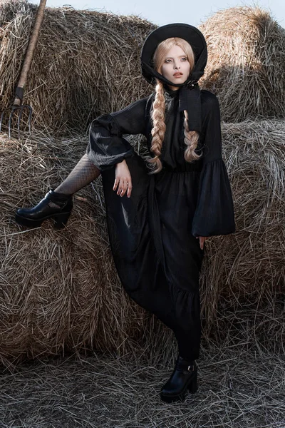 Fashion young woman wearing stylish black dress and hat at countryside. Amish fashion style. — Stock Photo, Image