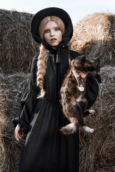 Mode jonge vrouw draagt stijlvolle zwarte jurk en muts op platteland. Amish fashion stijl. — Stockfoto