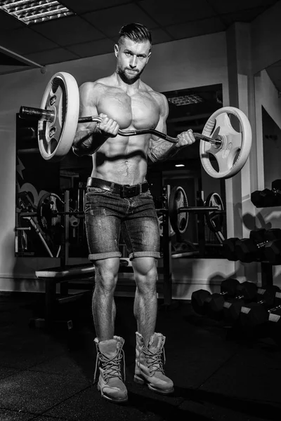 Atlético joven haciendo ejercicios con barra de pesas en el gimnasio. Guapo musculoso culturista chico está haciendo ejercicio. Imagen monocromática . — Foto de Stock