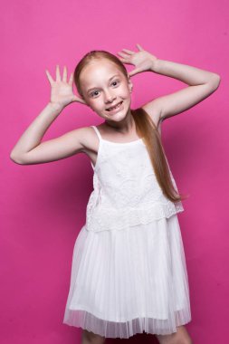 Model pembe bir arka plan üzerinde gibi poz beyaz elbiseli güzel küçük Kızıl saçlı kız.