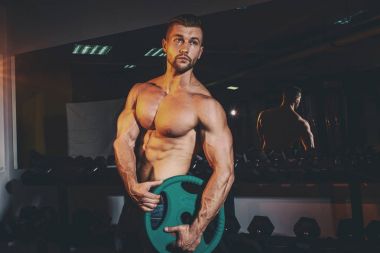 Kas pompalama ve spor salonunda eğitim kas güçlü atletik erkek. Halter alıştırmalar yapan yakışıklı vücut geliştirmeci adam. Vintage tonlama.