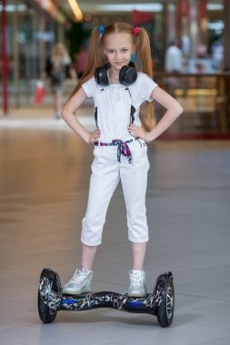 Mini segway alışveriş merkezi ticaret kulaklık üzerinde mutlu ve gülümseyen Kız biniyor. Vurgulu kurulu veya gyroscooter üzerinde sürme ve müzik genç.
