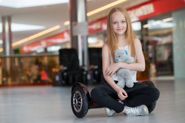 Mutlu ve gülümseyen kız mini segway ve Peluş ayı oyuncak bebek alışveriş merkezi ticaret ile. Vurgulu kurulu veya gyroscooter üzerinde sürme genç.