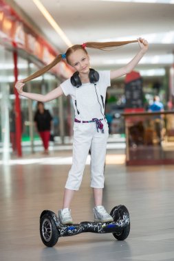 Mini segway alışveriş merkezi ticaret kulaklık üzerinde mutlu ve gülümseyen Kız biniyor. Vurgulu kurulu veya gyroscooter üzerinde sürme ve müzik genç.