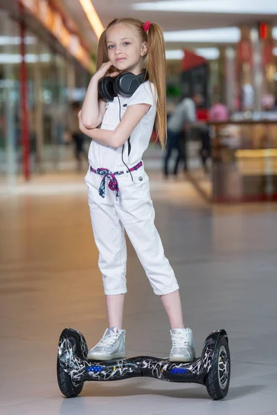 Boldog és mosolygós lány lovagol a mini segway a fejhallgató, a kereskedelmi mall. Tinédzser lovaglás légdeszkát vagy gyroscooter, és zenét hallgatni. — Stock Fotó