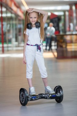 Mini segway alışveriş merkezi ticaret kulaklık üzerinde mutlu ve gülümseyen Kız biniyor. Vurgulu kurulu veya gyroscooter üzerinde sürme ve müzik genç.