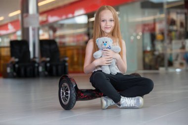 Mutlu ve gülümseyen kız mini segway ve Peluş ayı oyuncak bebek alışveriş merkezi ticaret ile. Vurgulu kurulu veya gyroscooter üzerinde sürme genç.