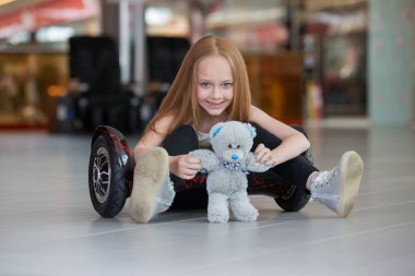 Mutlu ve gülümseyen kız mini segway ve Peluş ayı oyuncak bebek alışveriş merkezi ticaret ile. Vurgulu kurulu veya gyroscooter üzerinde sürme genç.