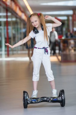 Mini segway alışveriş merkezi ticaret kulaklık üzerinde mutlu ve gülümseyen Kız biniyor. Vurgulu kurulu veya gyroscooter üzerinde sürme ve müzik genç.
