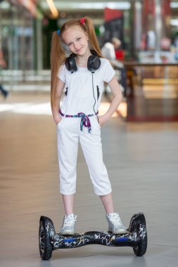 Mini segway alışveriş merkezi ticaret kulaklık üzerinde mutlu ve gülümseyen Kız biniyor. Vurgulu kurulu veya gyroscooter üzerinde sürme ve müzik genç.