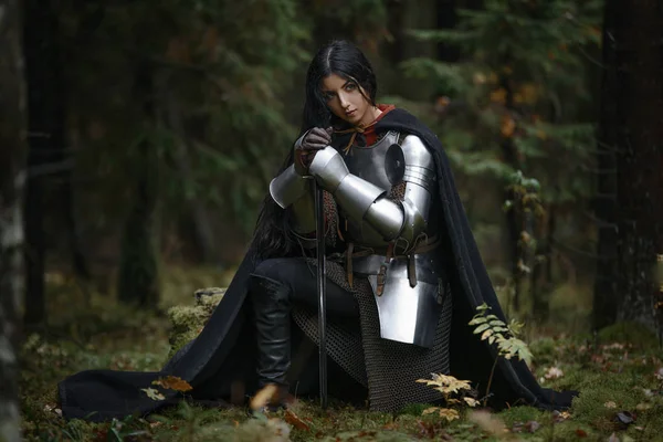 Una hermosa guerrera con una espada con cota de malla y armadura en un bosque misterioso . — Foto de Stock