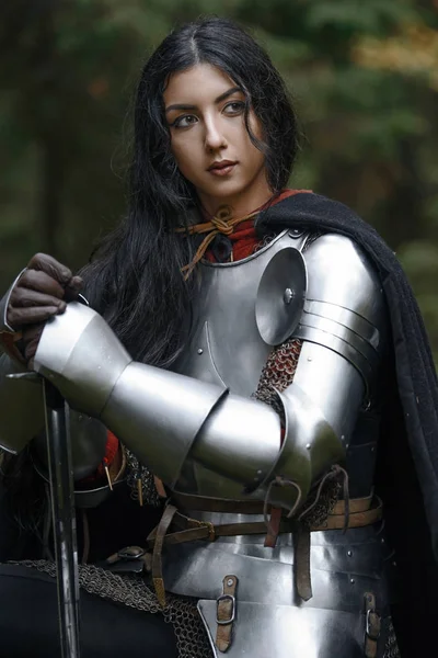 A beautiful warrior girl with a sword wearing chainmail and armor in a mysterious forest. — Stock Photo, Image