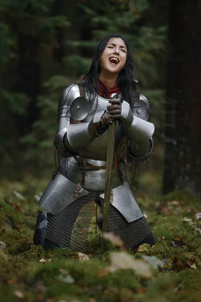 Una hermosa guerrera con una espada con cota de malla y armadura en un bosque misterioso . — Foto de Stock