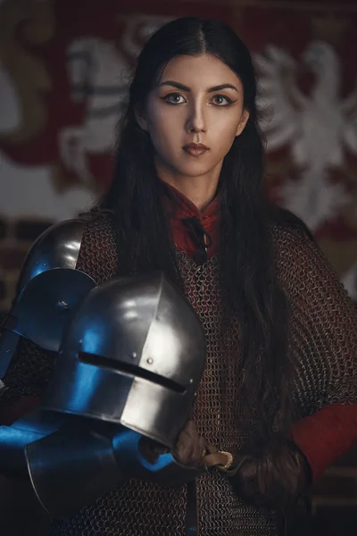 Retrato de una hermosa guerrera medieval en una capucha de malla con casco en las manos . — Foto de Stock