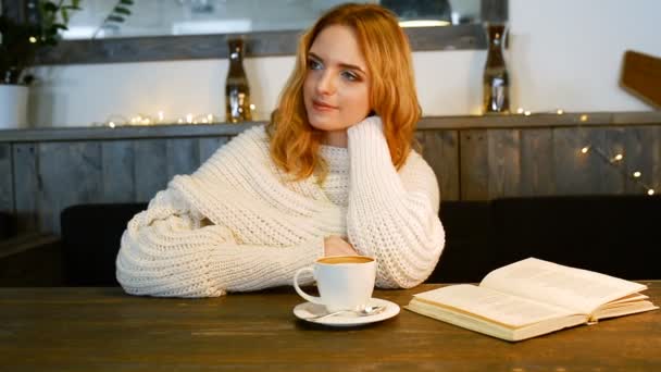 Joven hermosa mujer está leyendo un libro en la cafetería. Ella sonríe y disfruta del aroma del café . — Vídeos de Stock