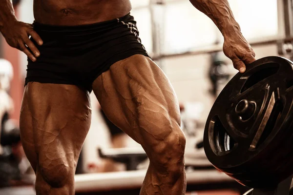 Primer plano de culturistas piernas musculares. Hombre atleta haciendo ejercicio en el gimnasio . — Foto de Stock